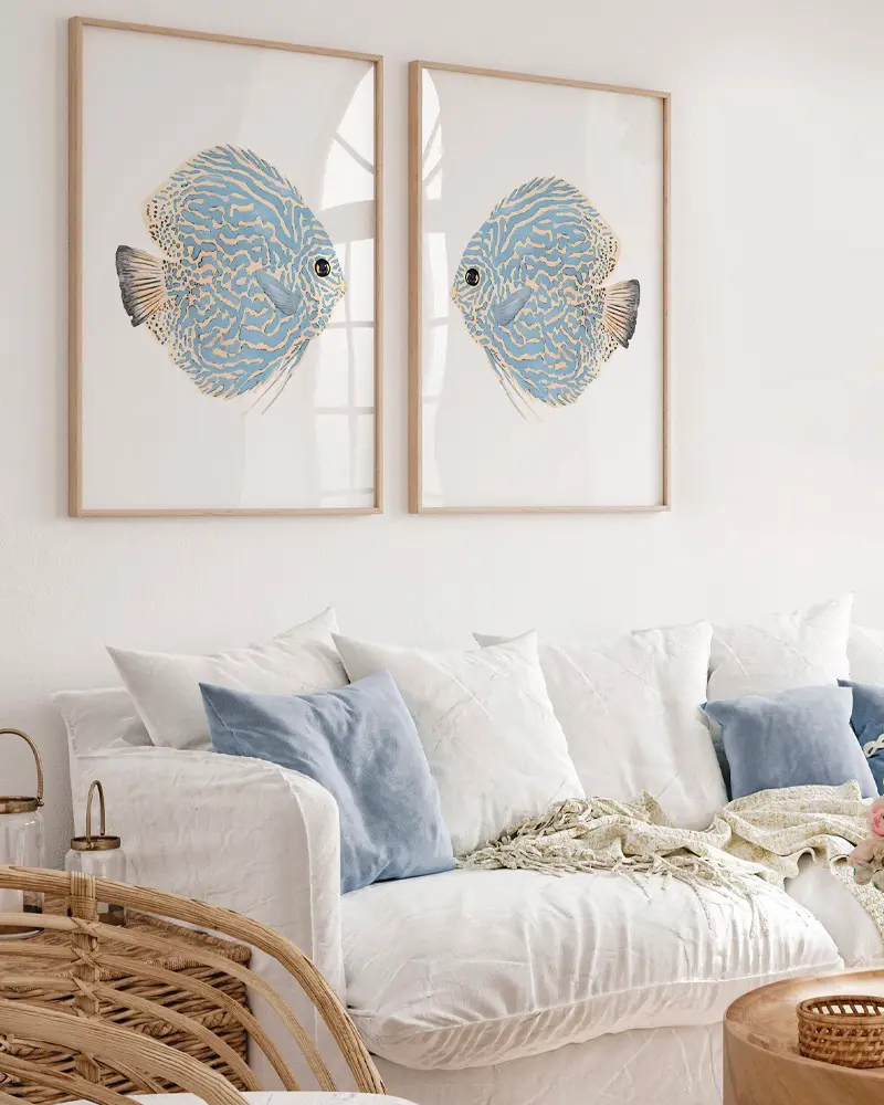 Pair of framed blue fish prints above a white linen sofa with blue and white pillows and a rattan chair