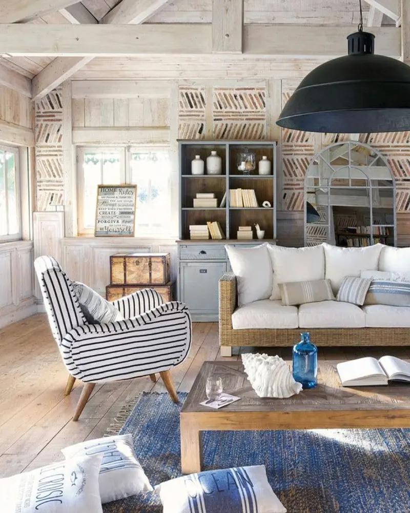 Whitewashed wood-paneled living room with a blue and white striped armchair, a white sofa, a wood coffee table, a blue rug and a black pendant