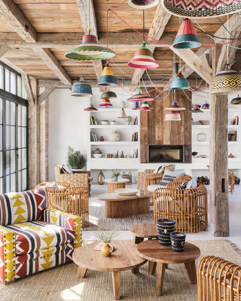 Large living room with colorful painted pendant lamps, rattan armchairs, patterned sofa and round wood tables
