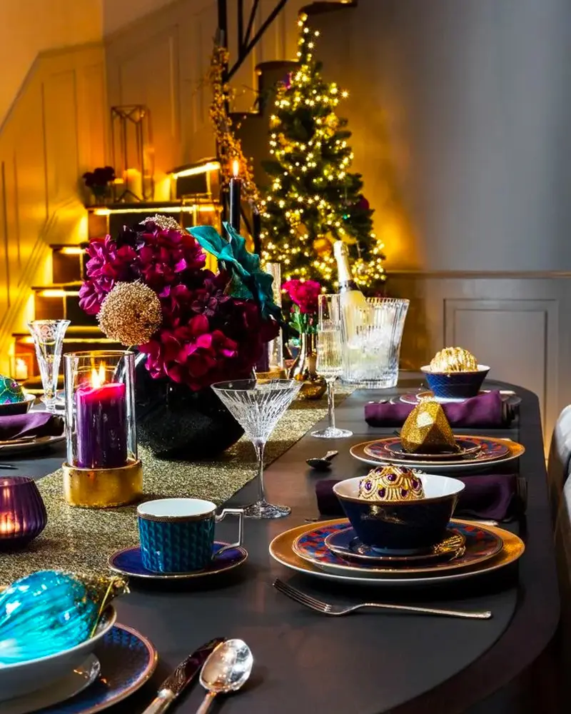 Festive dark table with jewel-toned flowers, gold-rimmed plates and colored glass