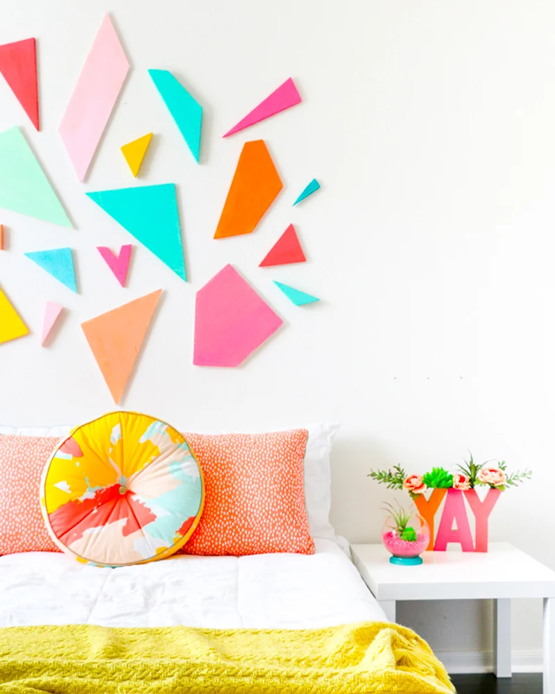 Bright foam geometric shapes in pink, coral and turquoise on the wall above a bed