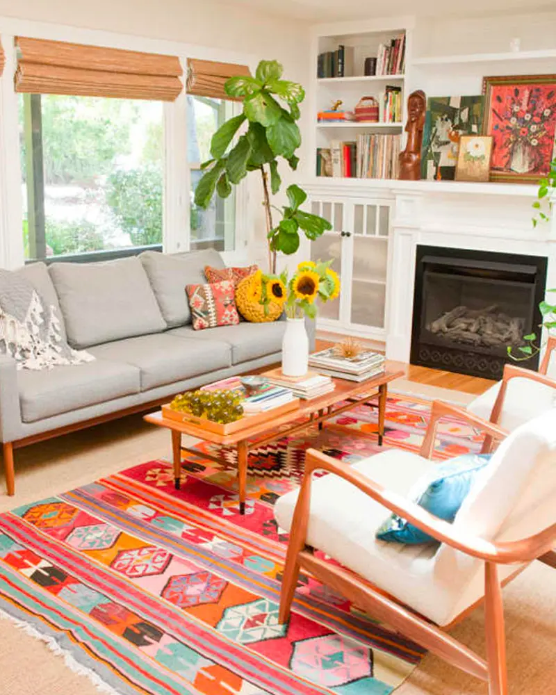 Gray mid-century sofa, colorful kilim rug, white armchair, fireplace and sunflowers
