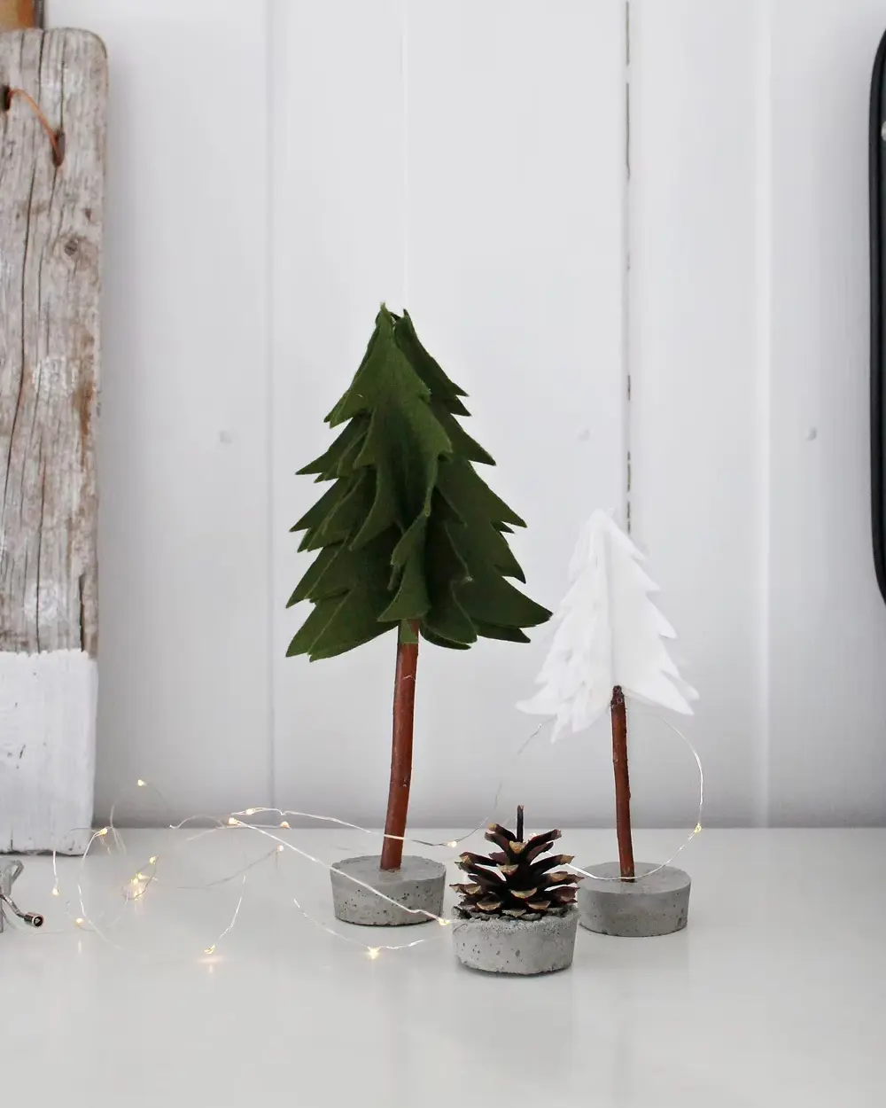 Two felt trees in green and white on twig trunks set in small concrete bases