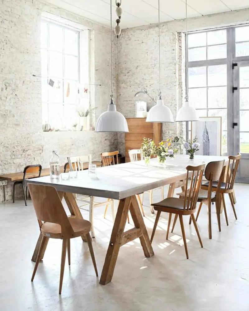 Long white table on wood trestle legs with white pendants, wood chairs and whitewashed brick