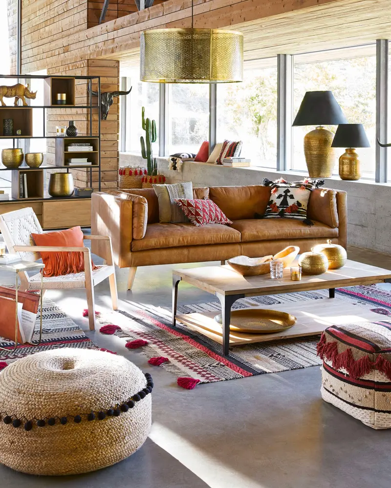 Cognac leather sofa, brass drum pendant, large poufs and colorful rug in an open space