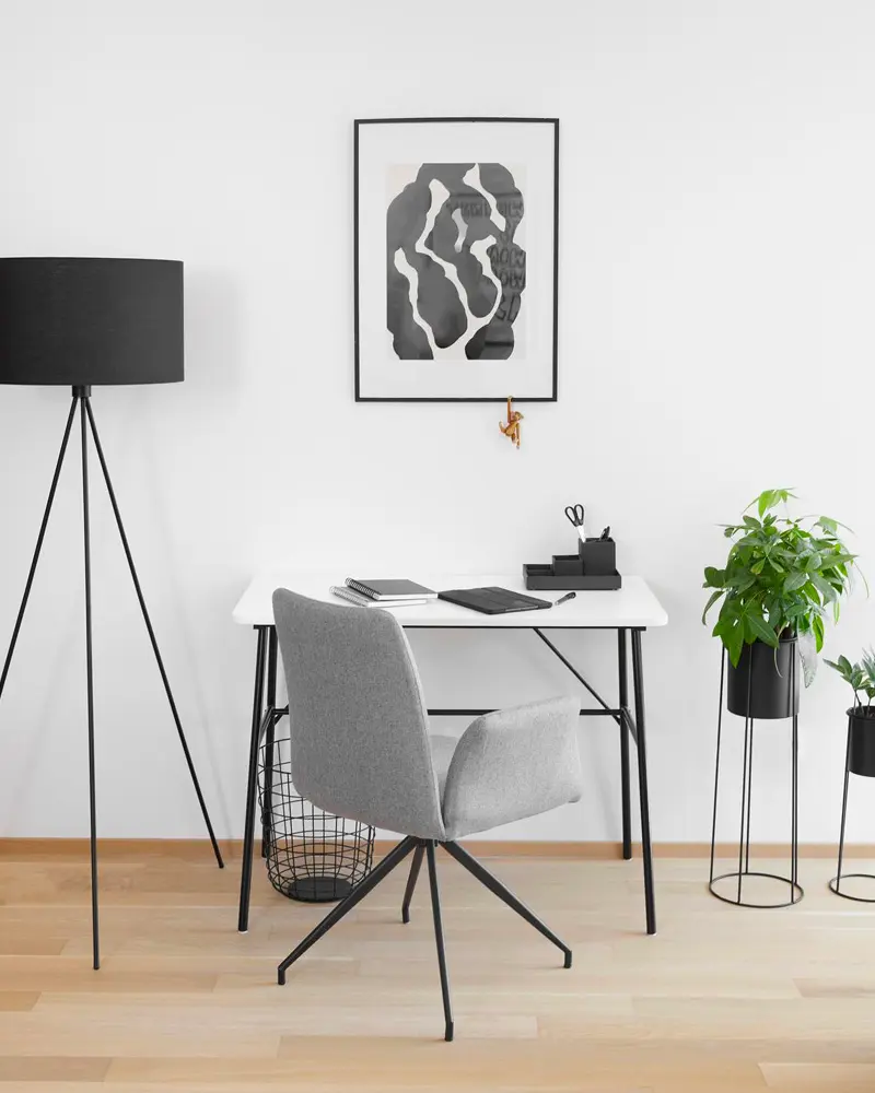 White desk with gray swivel chair, black tripod floor lamp, abstract black print and potted plant