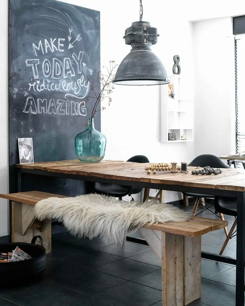 Wood table and bench with a sheepskin, a chalkboard wall and a gray factory pendant