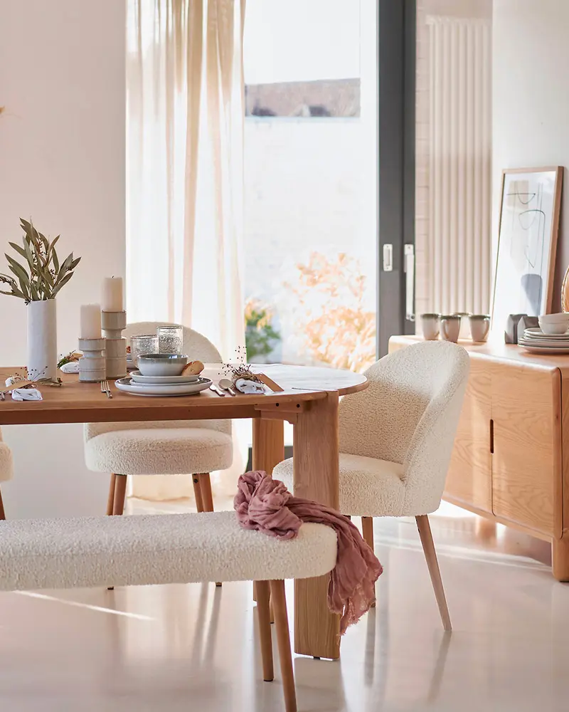 Wood dining table with boucle chairs and bench, linen curtains and ceramics