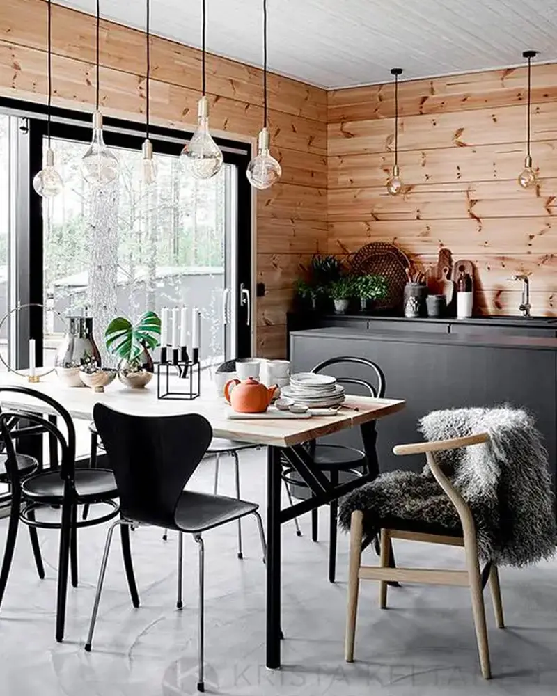 Pine-paneled wall, black chairs, sheepskin on a wishbone chair and glass bulb pendants