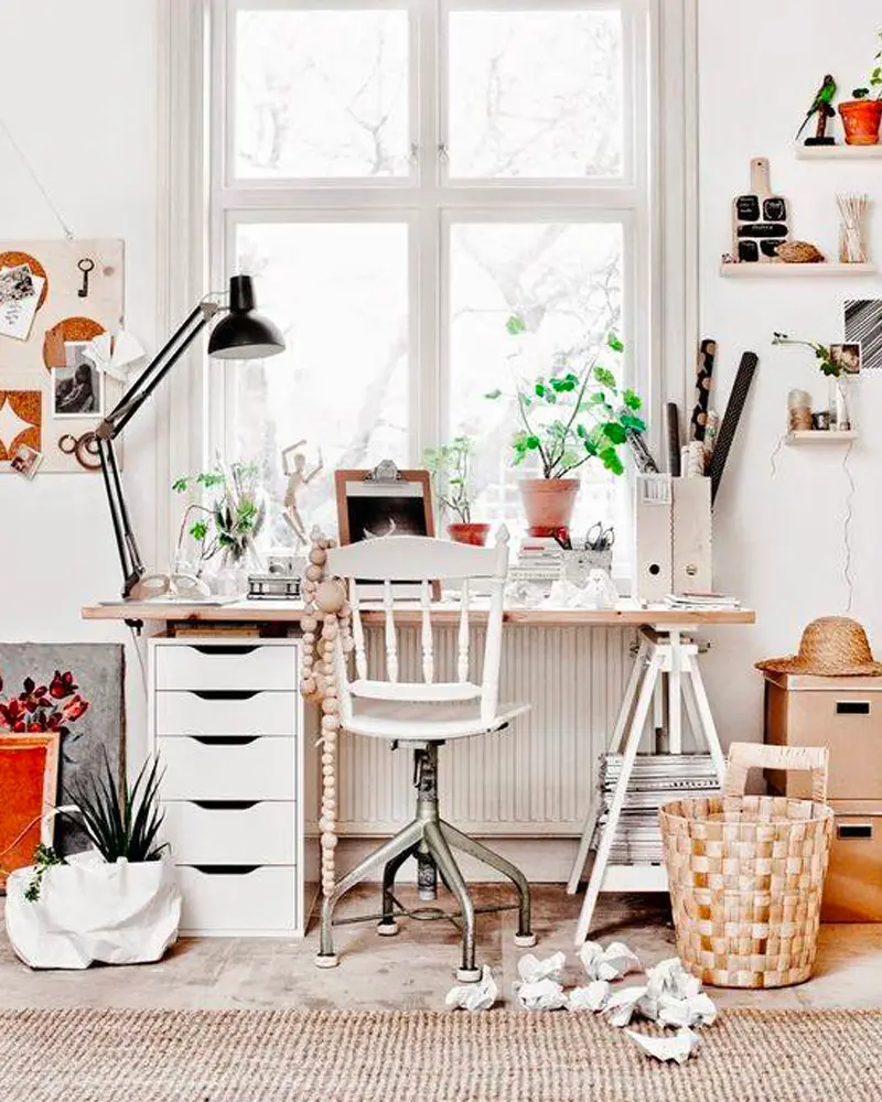 White desk with drawer unit, white spindle chair, black architect lamp, plants and pinned notes by a big window