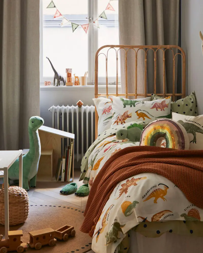 Kids bedroom with rattan bed, dinosaur print duvet, rust throw and plush dinosaur
