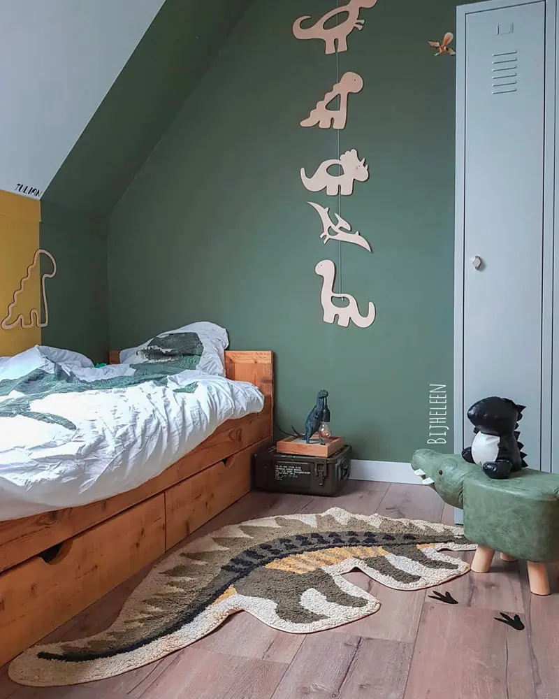 Kids room with sage wall, wooden bed, hanging wooden dinosaur cutouts and dinosaur-shaped rug