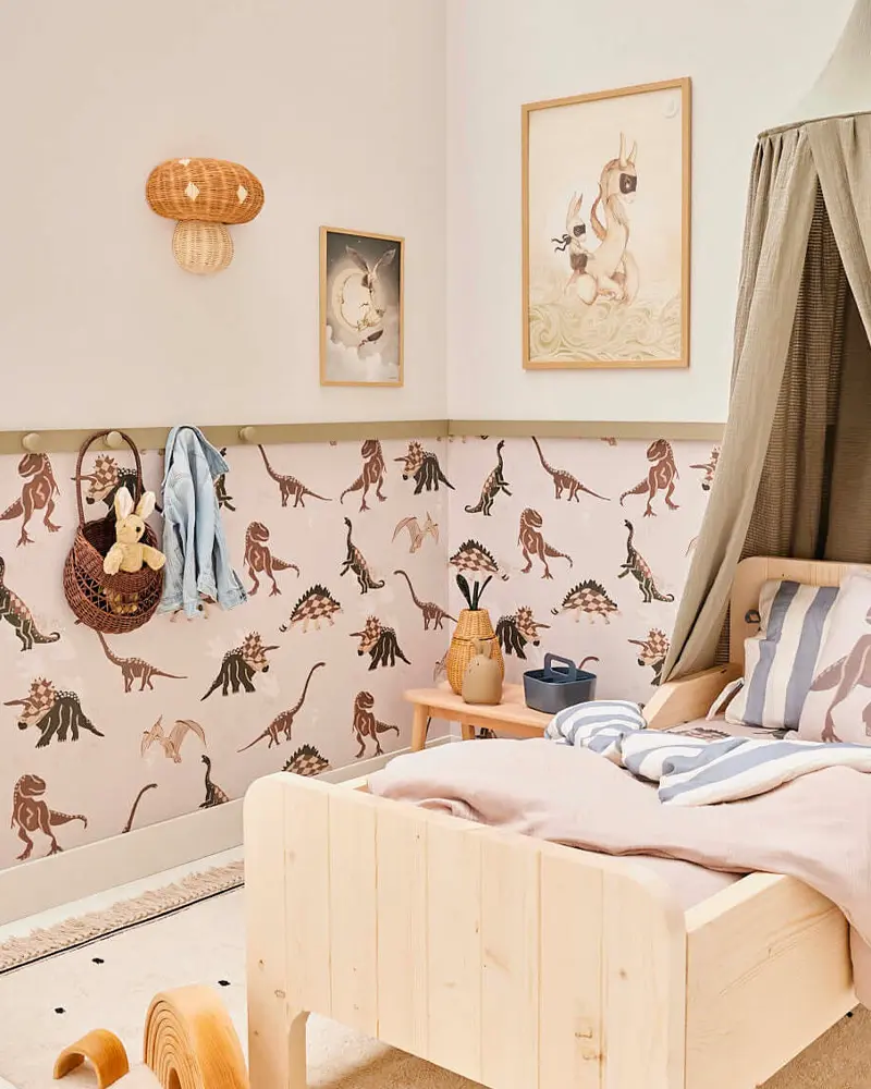 Kids room with dinosaur wallpaper below a chair rail, pine bed and canopy