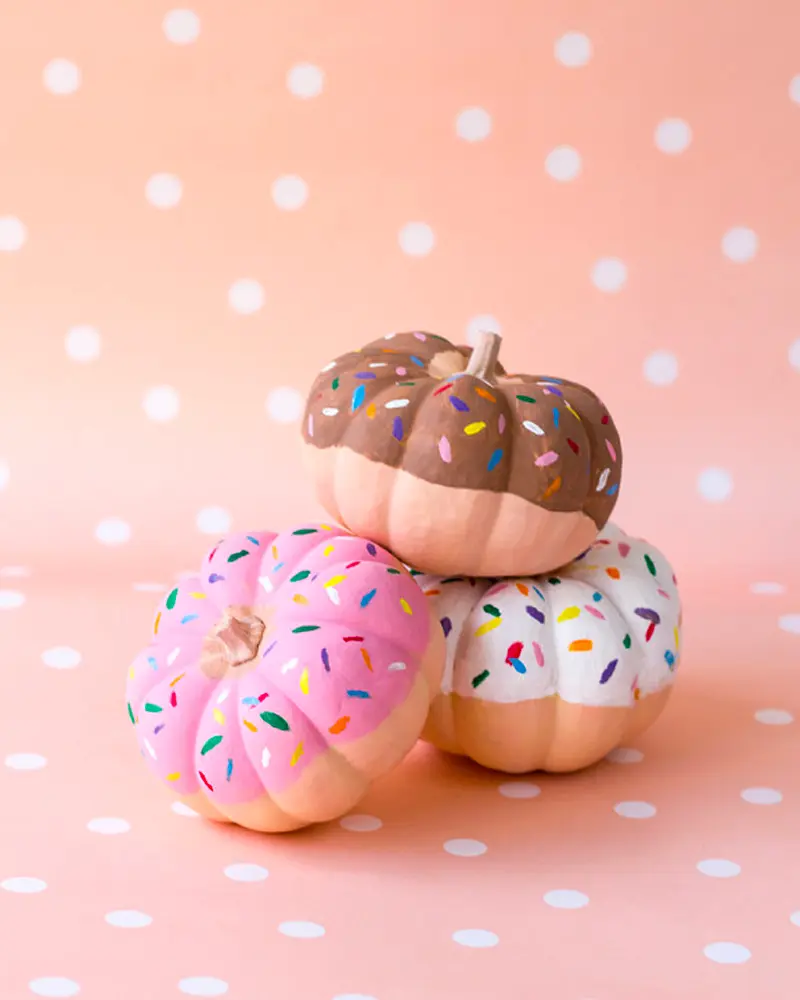 Three mini pumpkins painted as chocolate, pink and white frosted donuts with sprinkles