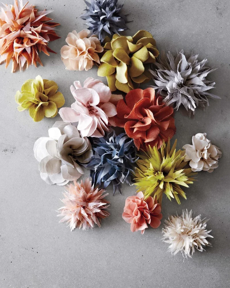 Assortment of fabric flowers in pink, olive, navy and gray on a concrete surface