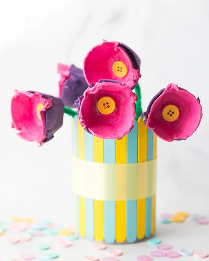 Pink egg carton flowers with yellow button centers in a striped popsicle-stick pot