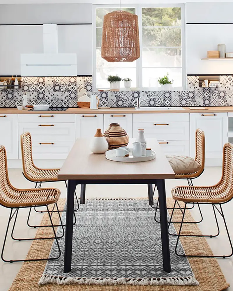 White kitchen with patterned cement tile backsplash, woven rattan pendant, rattan chairs and black table