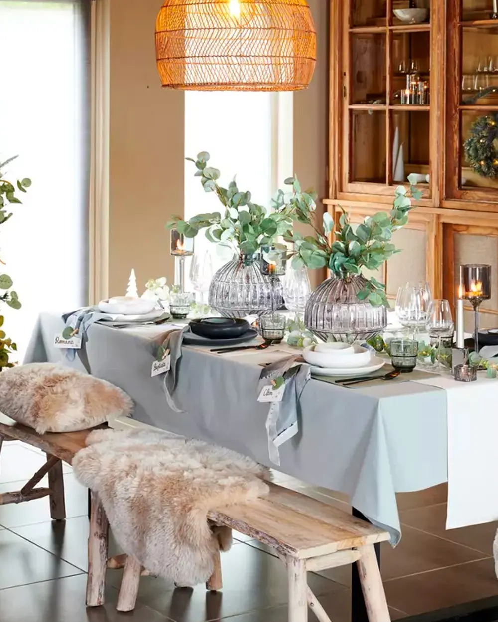Pale blue tablecloth with eucalyptus in glass vases, a wood bench with sheepskins and rattan pendant