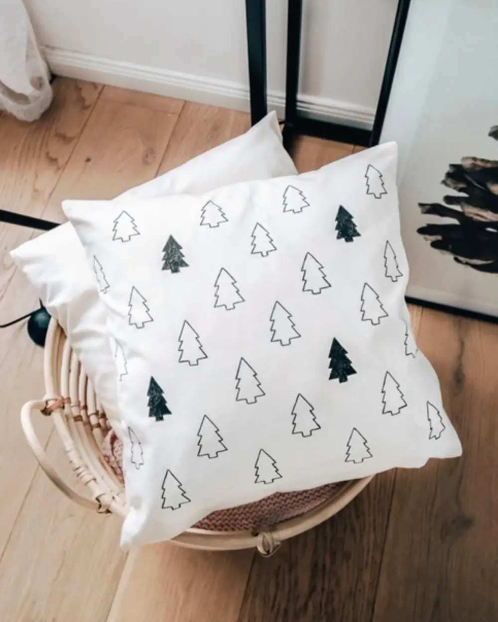 White pillow covered with hand-drawn Christmas tree outlines in black and green on a rattan chair