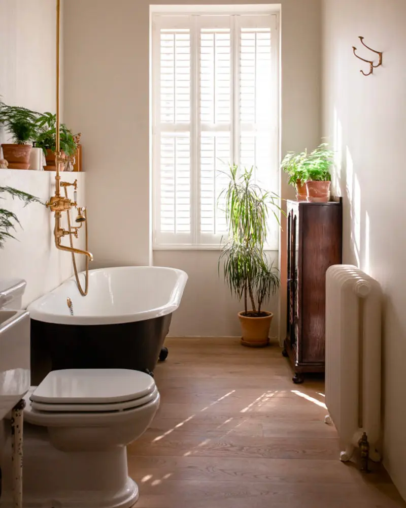 Bathroom with black clawfoot tub, shutters and plants