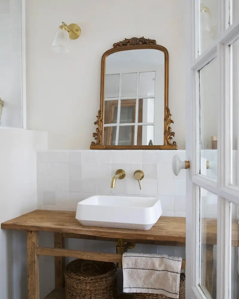Ornate gilded arched mirror over a rustic wood console vanity with a rectangular white vessel sink and brass wall faucet