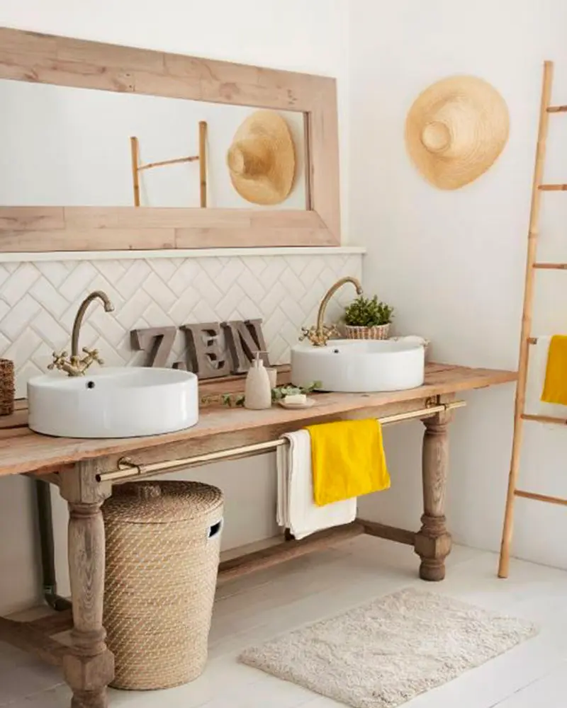 Rustic wood table turned into a double vanity with two white vessel sinks, a wood-framed mirror and straw hats on the wall