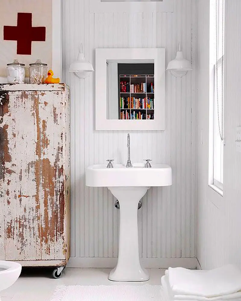White beadboard bathroom with a pedestal sink, a framed medicine cabinet, a chippy painted cabinet and a white sconce