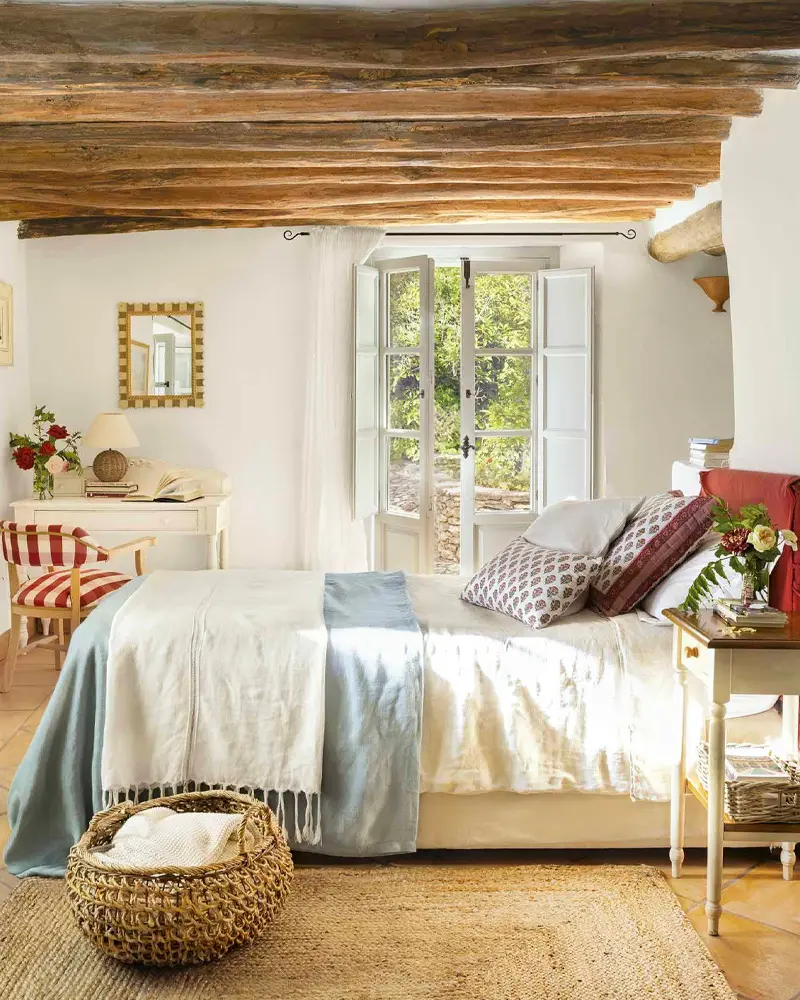 Dark wood beams, a pale blue throw, red striped chair and a wicker basket in a sunny bedroom