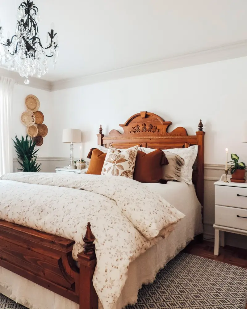 Carved antique wood bed with a floral duvet, rust pillows and a black crystal chandelier