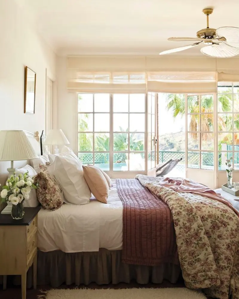 Floral quilt and a burgundy blanket on a bed in a sunny bedroom with tall windows and a ceiling fan