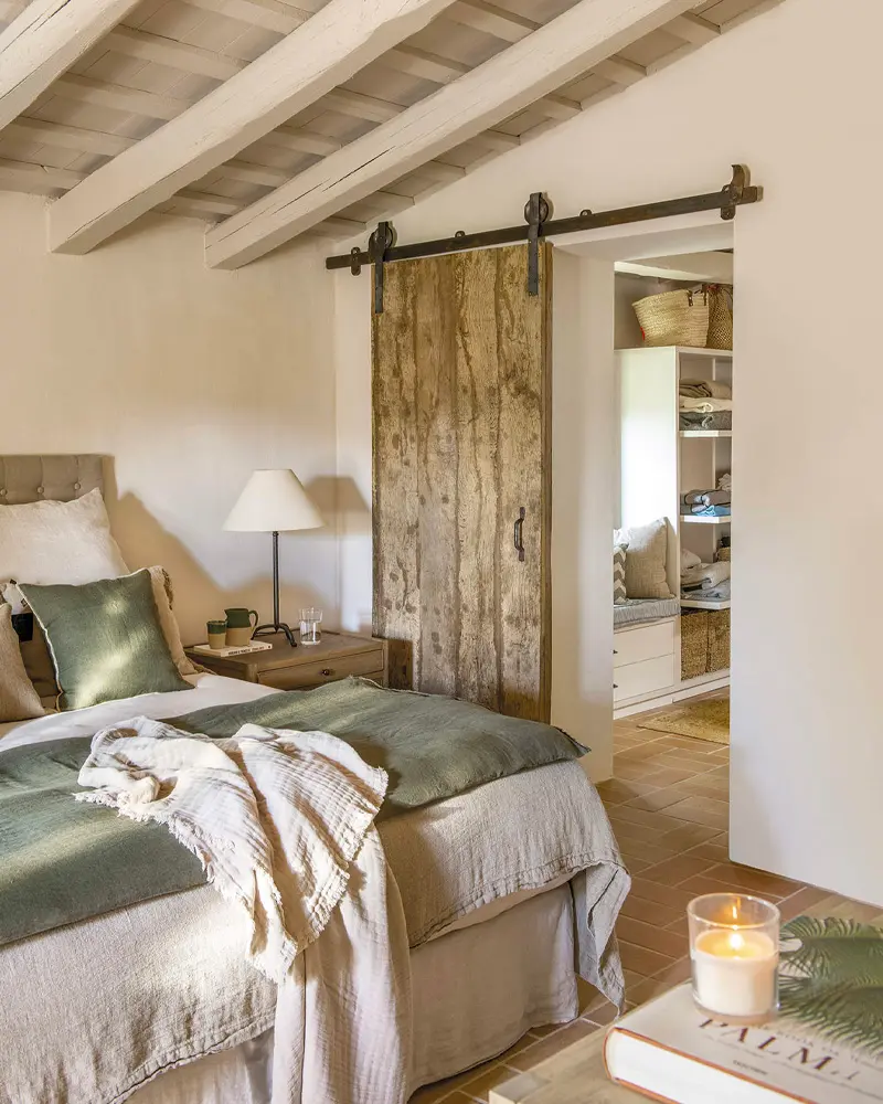 Sage green and white bedding, a sliding barn door and a beamed ceiling in a cream bedroom