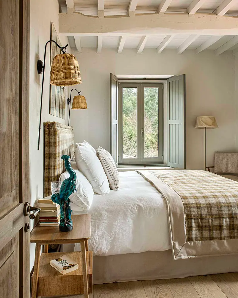 Plaid bedding, a checked headboard, rattan wall sconces and gray-green shutters in a white bedroom