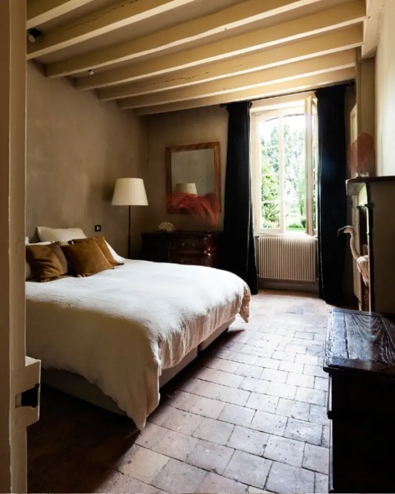 Dim bedroom with a terracotta brick floor, beige walls, a white bed and navy curtains