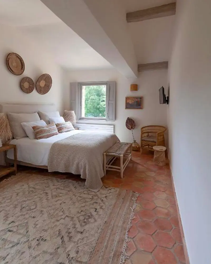 Hexagonal terracotta floor tiles, a woven rug and woven baskets on the wall in a simple bedroom