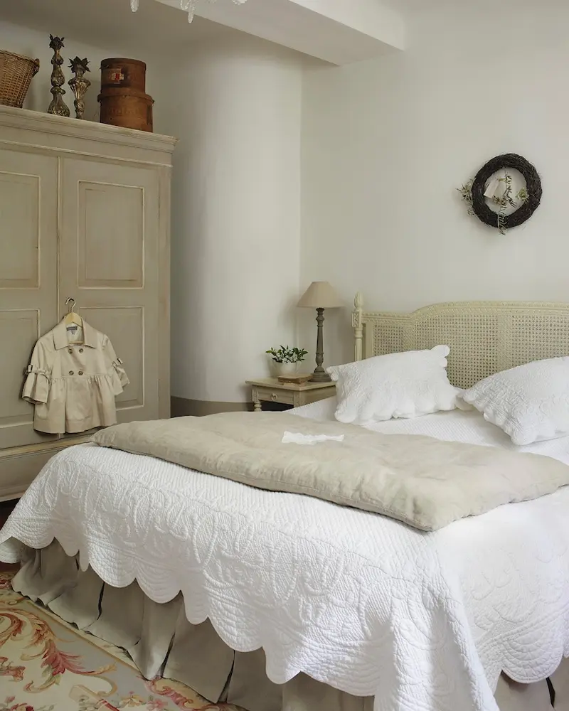 Cane headboard, a scalloped white quilt, a painted armoire and a round wall clock