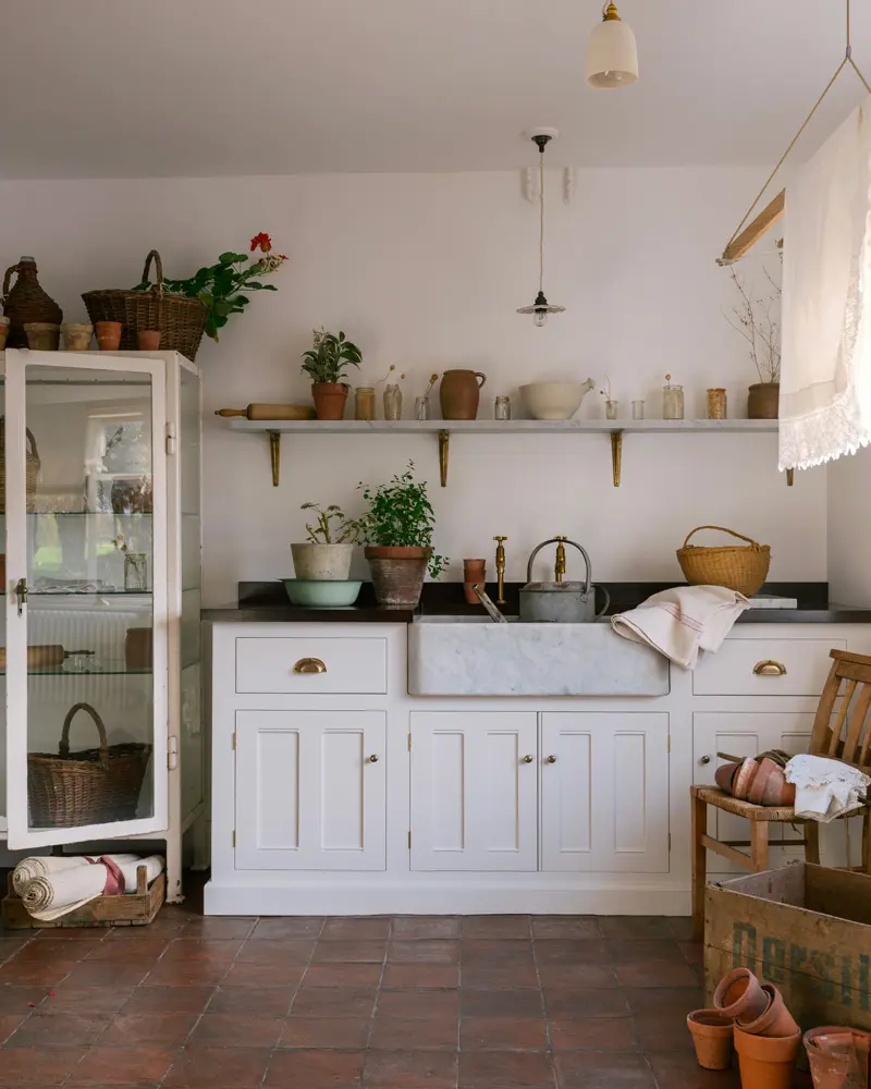 White cabinets, a glass display cabinet and terracotta floor tiles in a sunny country kitchen