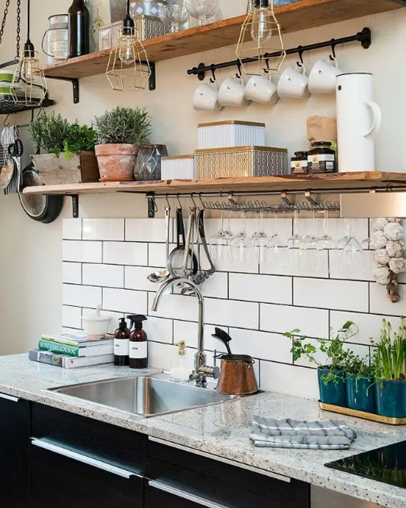 Wood shelves on black brackets with mugs on a rail above white subway tile and a steel sink