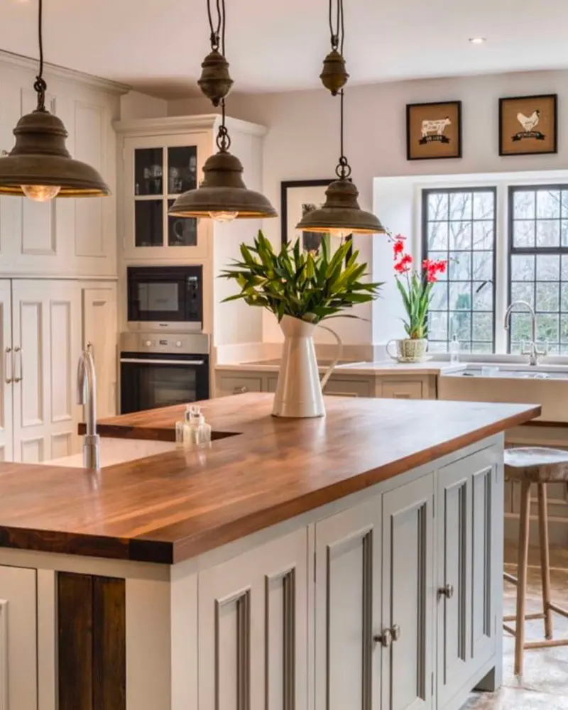 Three metal pendant lights over a walnut-topped island with a jug of tulips