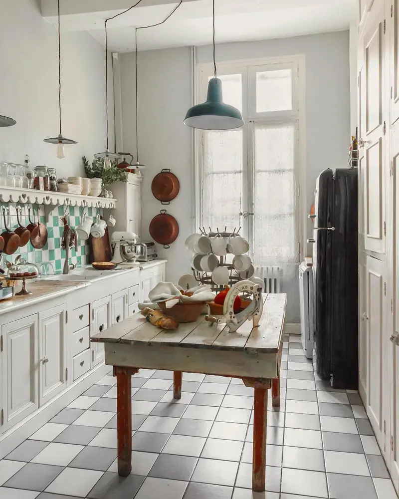 Teal enamel pendant, copper pans and a rustic wooden table in a white country kitchen