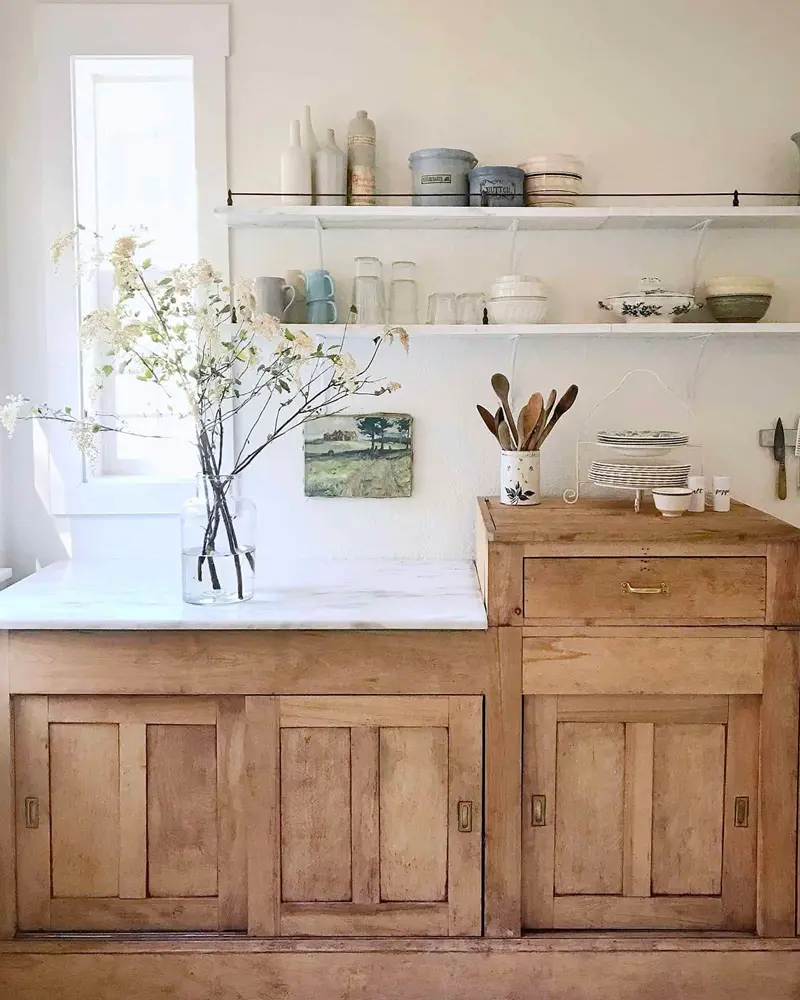 Antique pine cupboard with a marble top below simple white shelves of pottery
