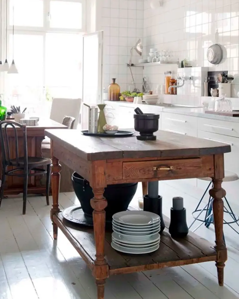 Antique wooden worktable with turned legs used as an island in a white kitchen