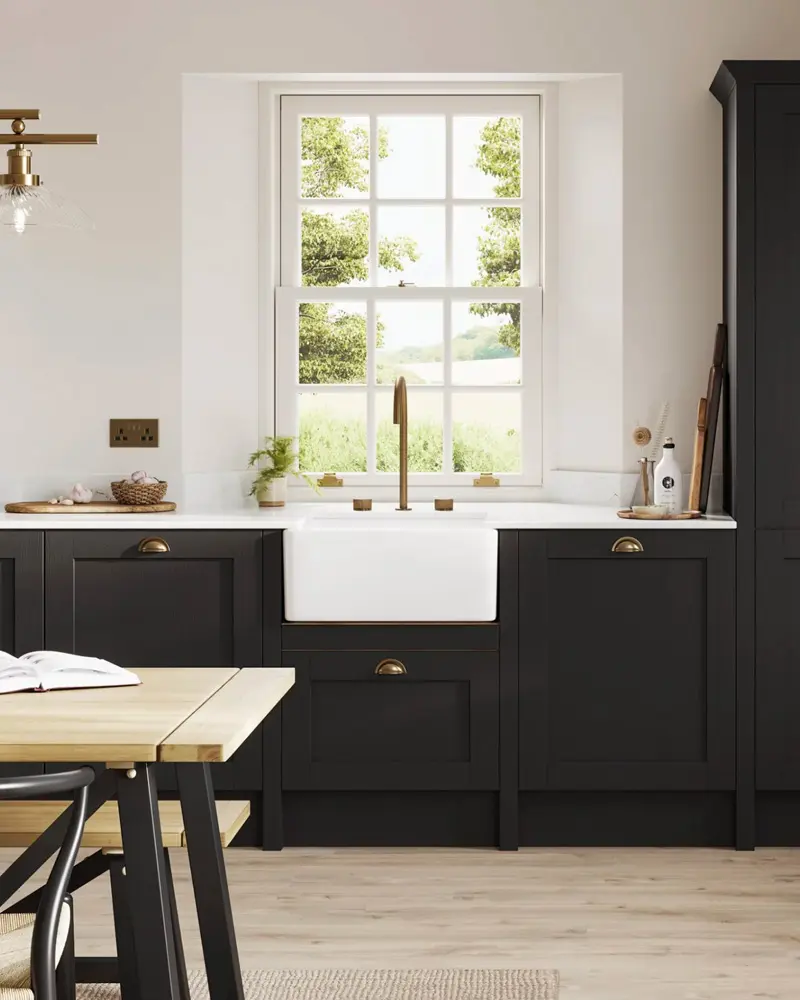 Black shaker cabinets, a white apron sink and a brass faucet below a sash window