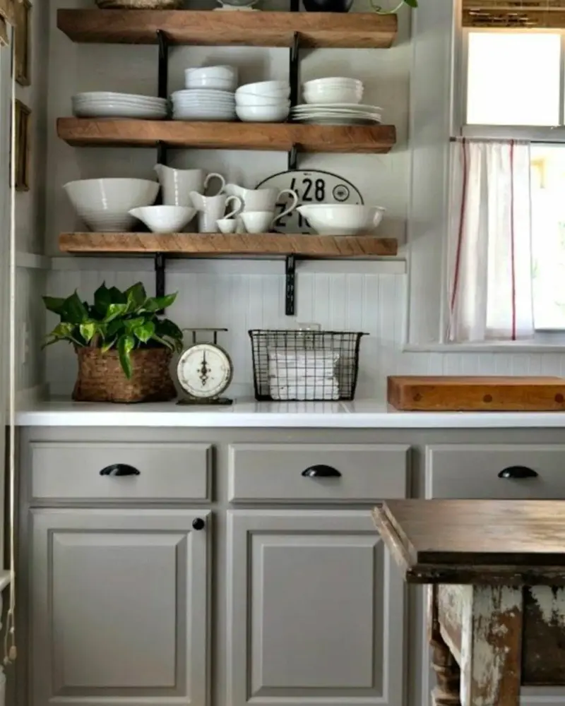Gray painted cabinets with cup pulls under reclaimed wood shelves of white dishes