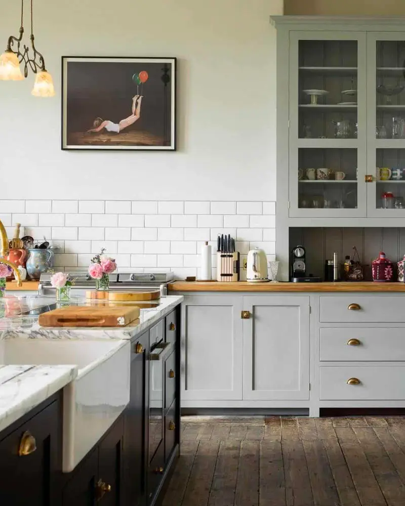 Gray-green glass-front hutch, subway tile and a marble-topped island in a farmhouse kitchen