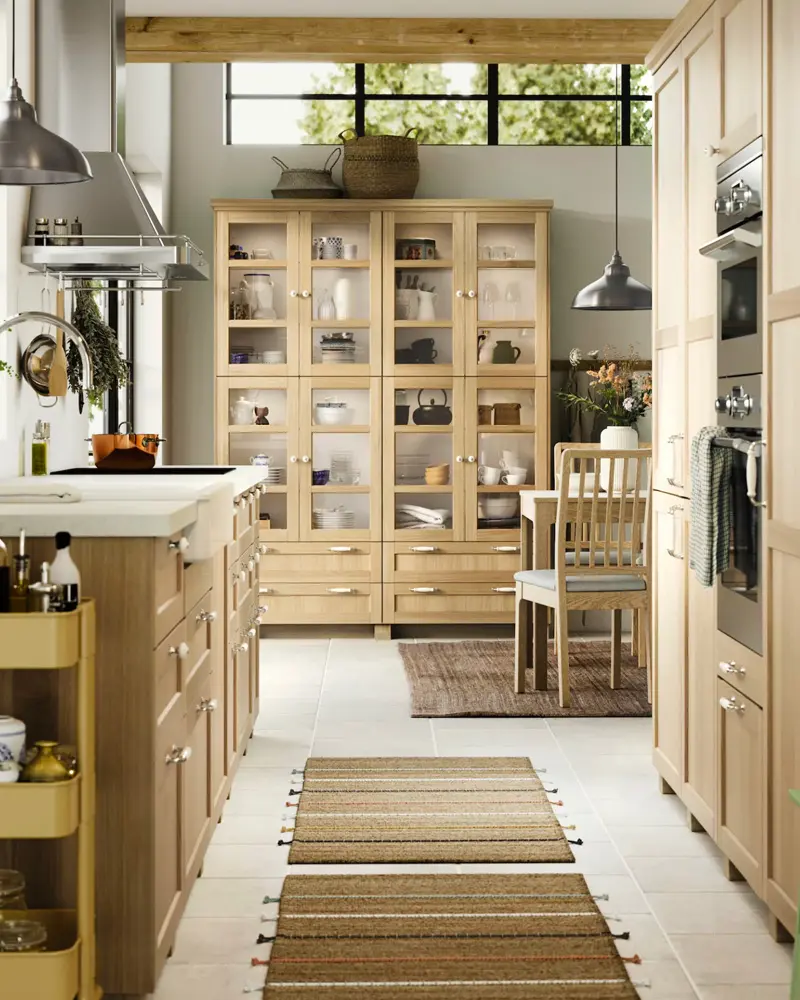 Oak glass-front pantry hutch, a striped runner and black pendant lights in a long farmhouse kitchen