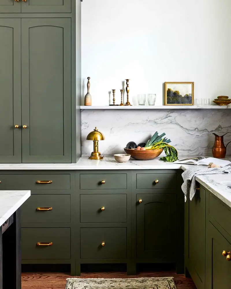 Olive green cabinets with brass knobs, a marble backsplash and a ledge of candlesticks