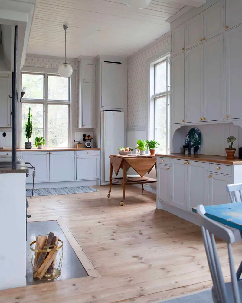 Pale gray-blue cabinets, butcher-block counters and a wide pine floor in a bright Scandinavian farmhouse kitchen