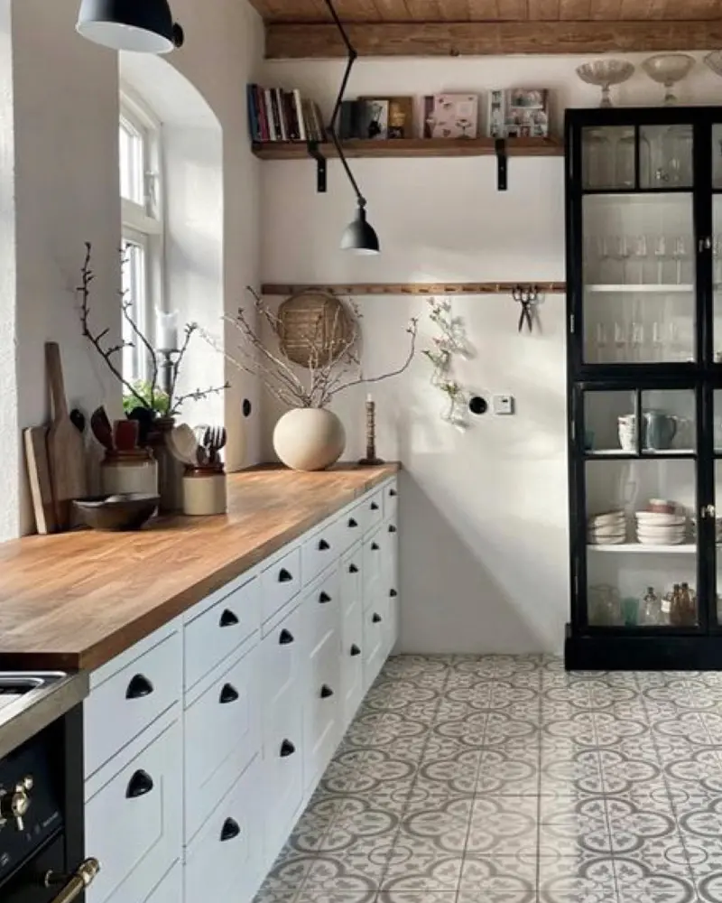 White cabinets with a butcher-block counter, a black glass cabinet and patterned cement floor tile