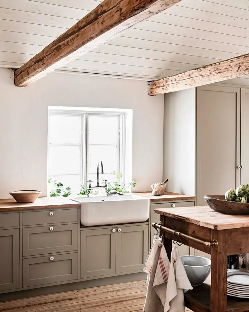 Taupe shaker cabinets, a farmhouse sink and a rustic wood island under weathered ceiling beams
