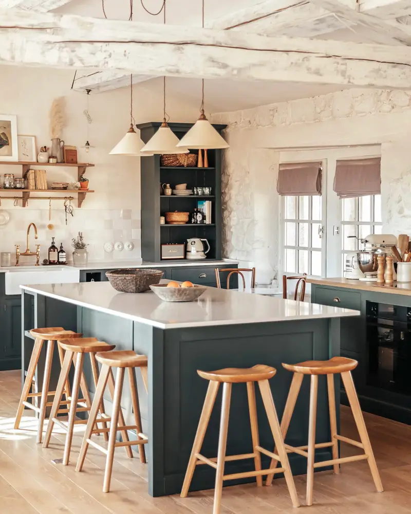 Dark teal island with wooden stools under three pendant lights in a whitewashed country kitchen